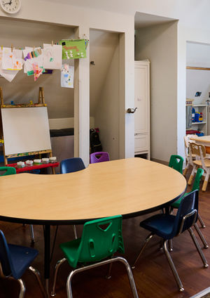 An arts & crafts table sits in front of an easel and hung children's art in a large classroom