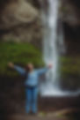 Woman standing in front of waterfall, holding bottle of Broken Top Whiskey.