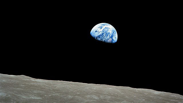 A photograph of the earth in a black sky above the gray moon landscape horizon
