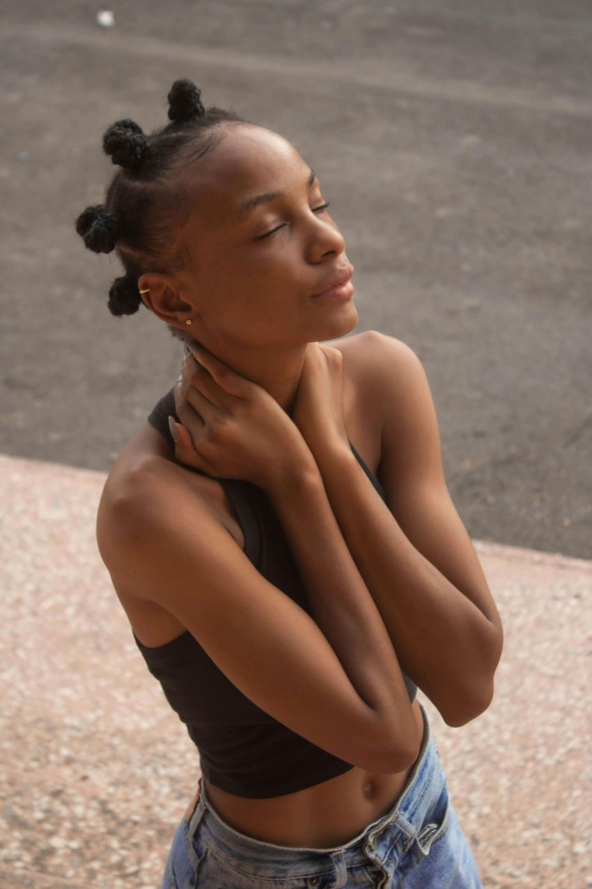 Schwarze Frau mit Lockenfrisur fäst sich am Halz und sieht in den Himmel