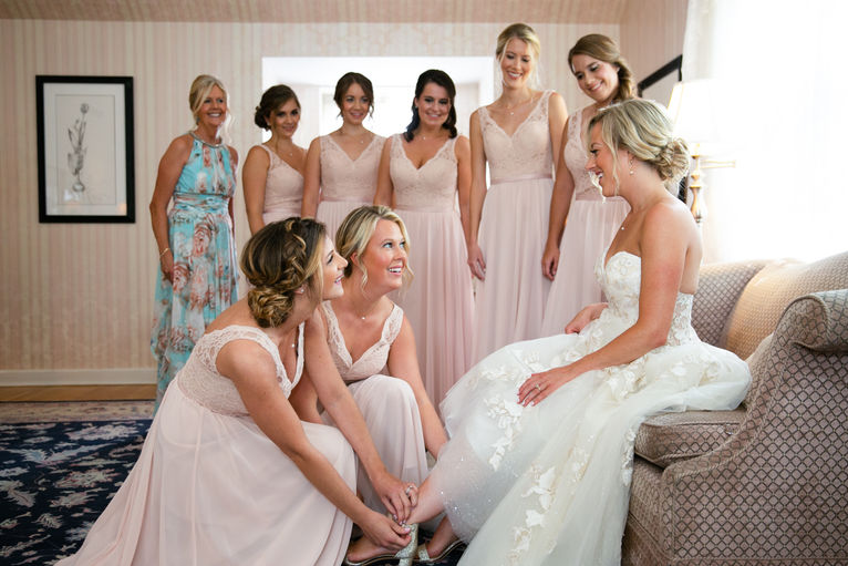Bridesmaids helping the seated bride with her wedding shoes