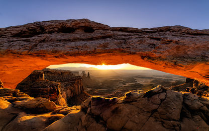 O belo nascer do sol no Mesa Arch, com seu "glow" laranja vibrante sob sua abertura, emoldurando a atmosfera mágica do relevo do vale abaixo, Canyonlands National Park, Utah