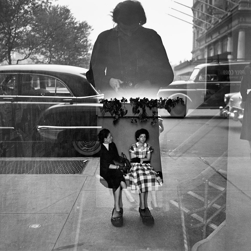 Fotografia de Vivian Maier. Mulher se fotografa no reflexo de uma vitrine.