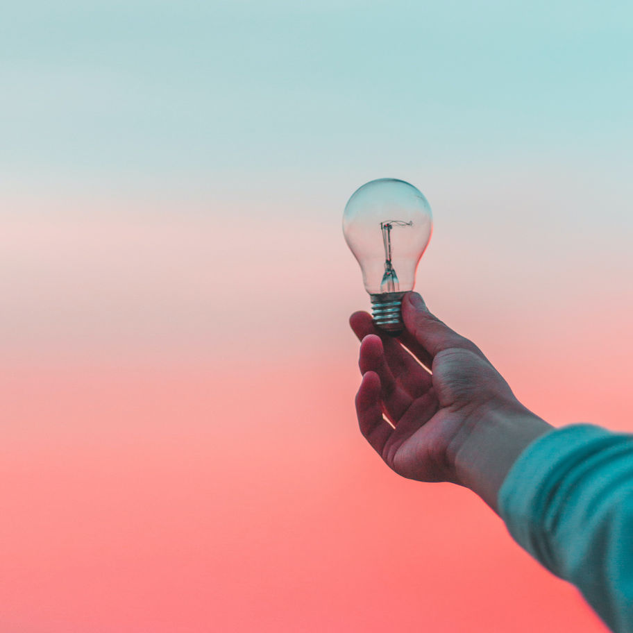 A person holding up a light bulb outside, with a sunset background