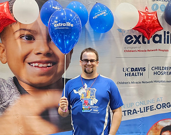 A man stands with a smile as his hand is in his pocket and the other hand is holding three balloons
