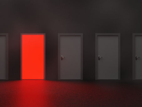 Fünf Türen in einem dunklen Raum, eine leuchtet rot: Bild für Entscheidungsangst und die Qual der Wahl