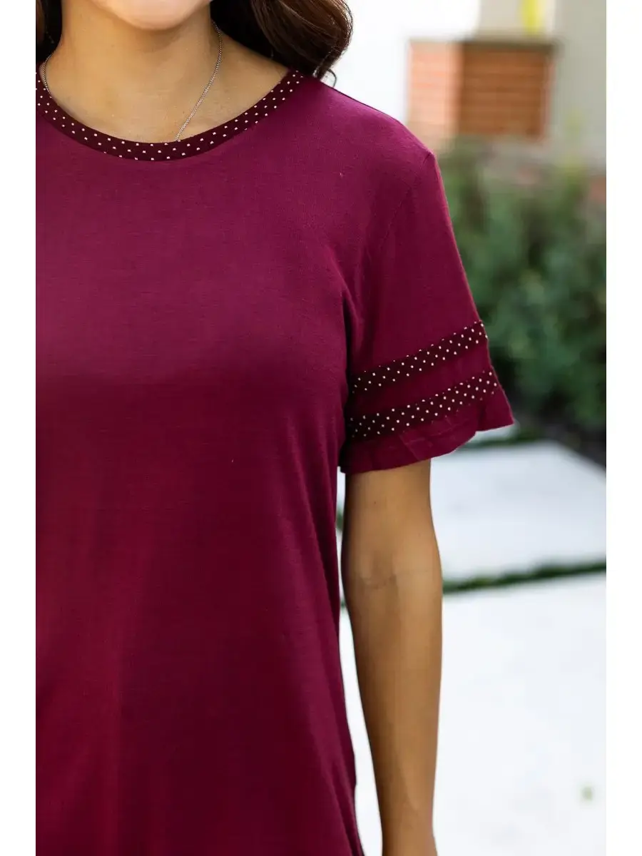 "Model wearing a burgundy tunic top with polka dot detailing on the sleeves and neckline, standing outdoors."