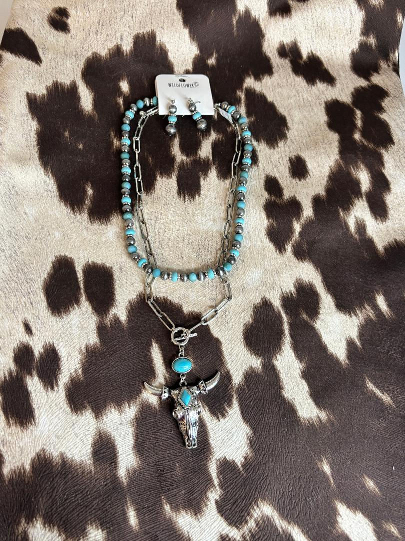 Western turquoise beaded and silver chain necklace with steer skull pendant and matching earrings on cowhide background