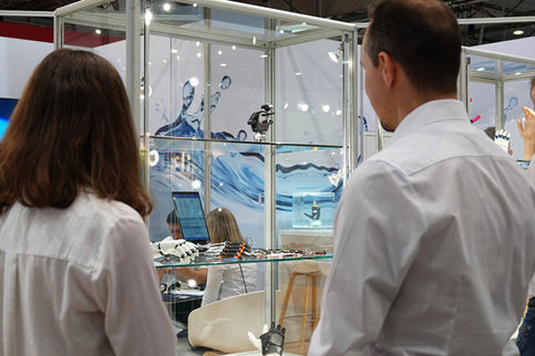 Zwei Personen betrachten eine Präsentation von Handprothesen in einer Glasvitrine auf einem Messestand