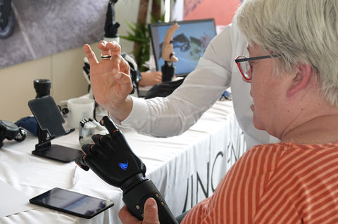 Demonstration myoelektrischer Hand- und Partialhandprothesen auf einem Tisch, während zwei Personen die Systeme erläutern und vergleichen