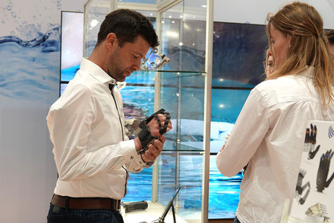 Eine Person demonstriert die Funktion eines Exoskeletts an einem Messestand, während eine weitere Person zusieht