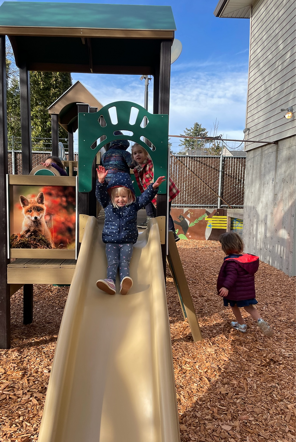 DiscoveryLand children playing in and around play structure, center child is sliding down a slide.