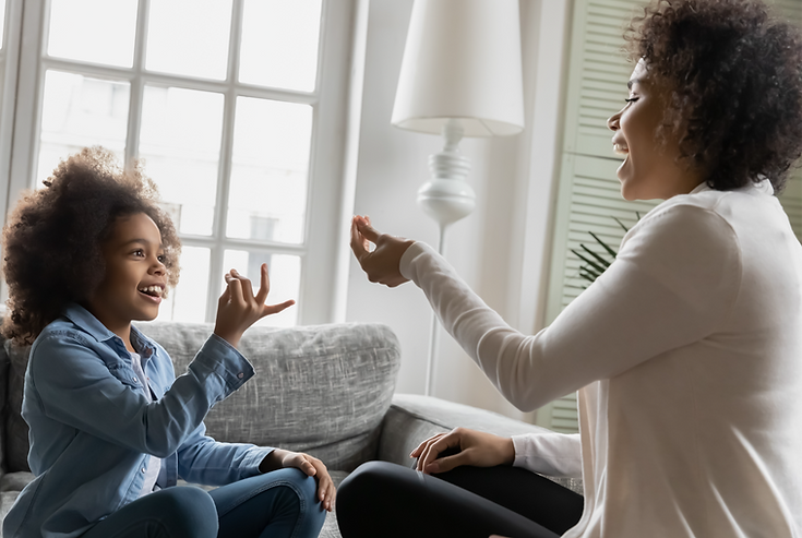 Female child care provider smiling and making a hand gesture to a young girl who is also smiling and making a hand gesture.