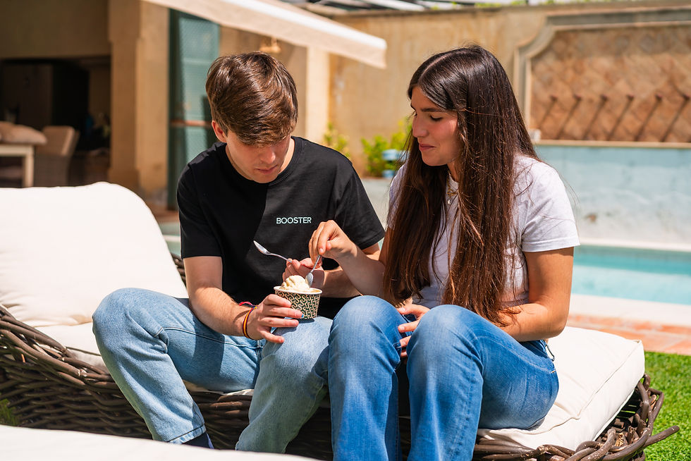 Dos jóvenes sentados al aire libre junto a una piscina, compartiendo una tarrina de helado.