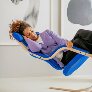 Frau liegt entspannt im Gravity™ Schwebesessel von Varier – natürliche Erholung, blaues Polster, Holzgestell Esche natur