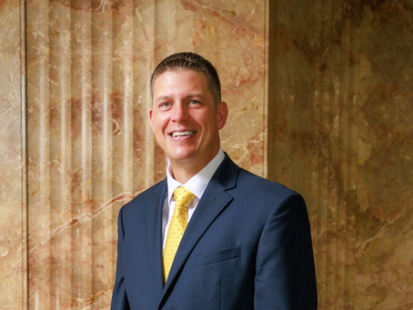 A man in a dark suit standing in front of a marble backgroundatue.