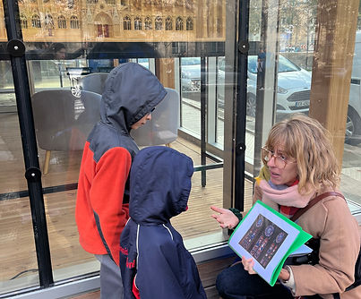 A woman is crouched on the ground and showing two children an image of stained glass windows