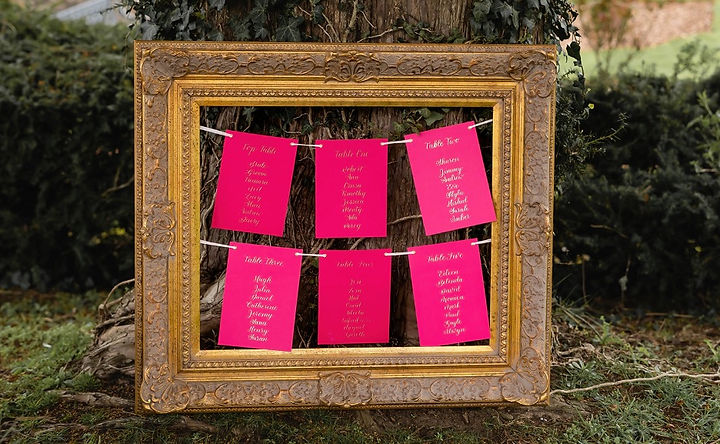 hand lettered calligraphy table plan - gold calligraphy on hot pink card suspended in an antique frame hand lettered calligraphy table plan - gold calligraphy on hot pink card suspended in an antique frame