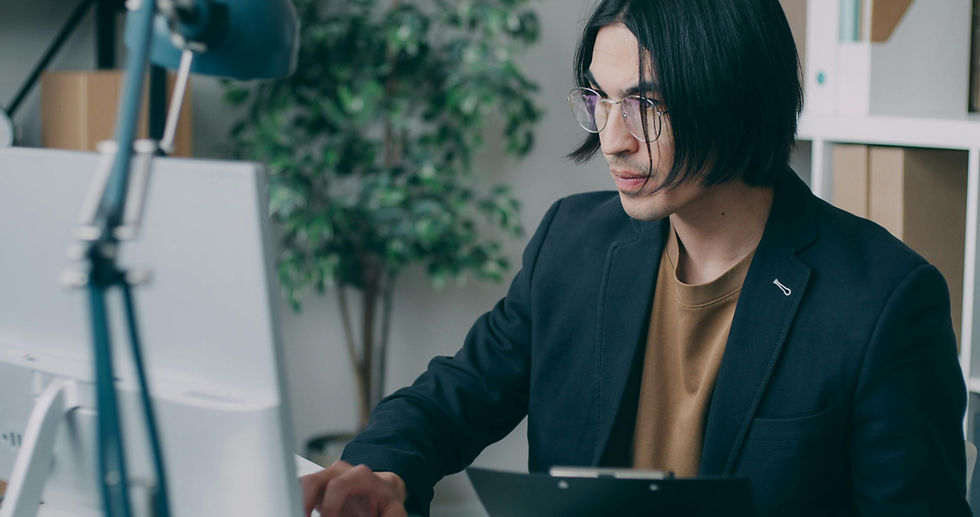 An assistant in glasses and blazer works intently at a desk with a computer.