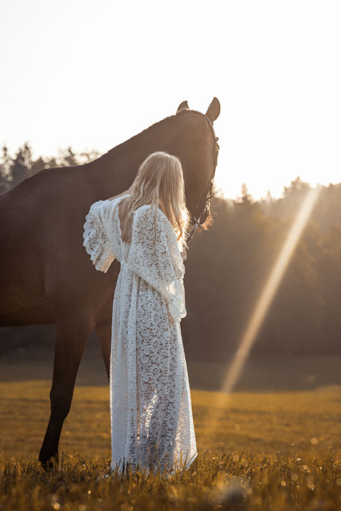Pferd und Reiterin stehen nebeneinander und betrachten in einer Sommerwiese den Sonnenaufgang.
Pferdefotografie von Saskia Ann Fotografie