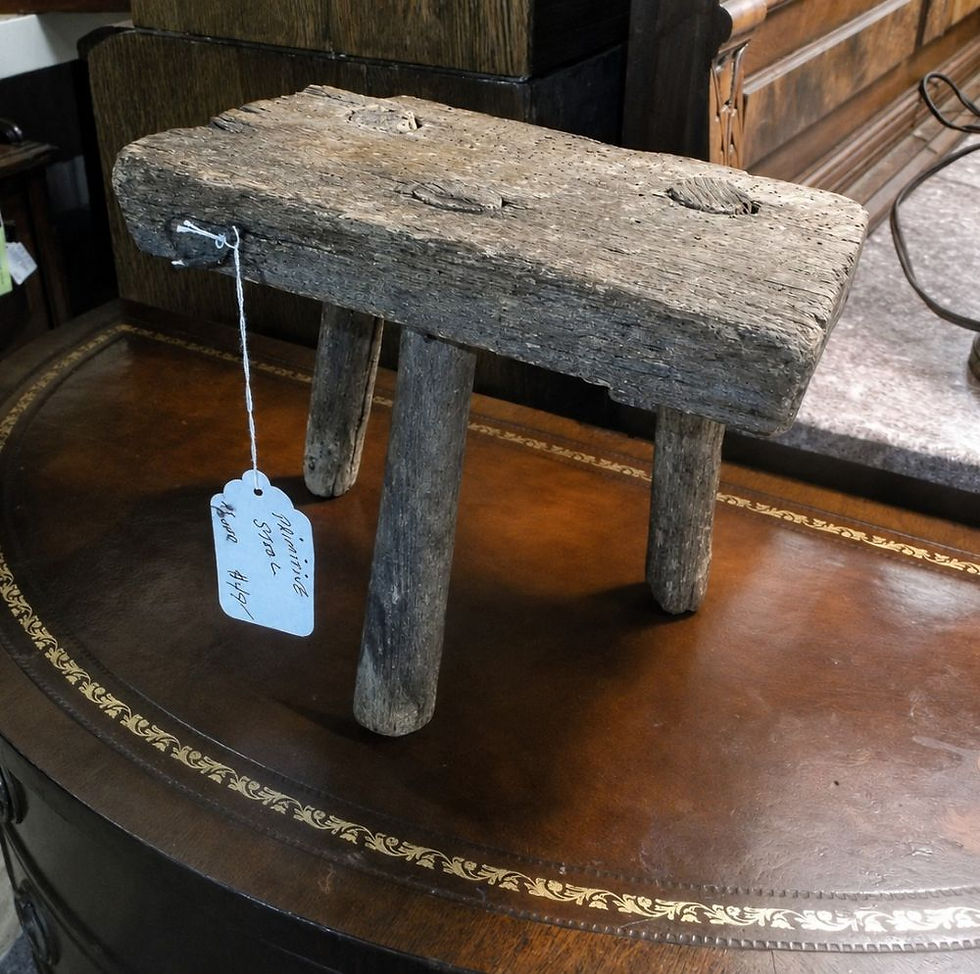 Weathered gray-brown primitive wooden stool with a thick plank seat and 3 peg legs.
