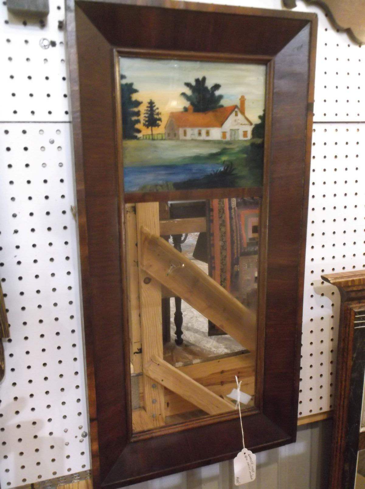 Large dark reddish-brown ogee mirror with a painted country house scene above the glass, displayed on green grass.