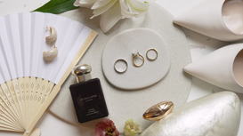 Wedding flatlay with engagement ring wedding bands Jo Malone perfume earrings petals and bamboo fan.
