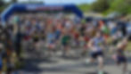 A picture of masses of individuals participating in the fun run. They are dressed in exercise clothing and running shoes. They have just run past the start line. It is a sunny day.
