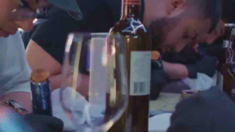 two people practicing drawing with tattoo-style pens, with a bottle of wine in front of them.