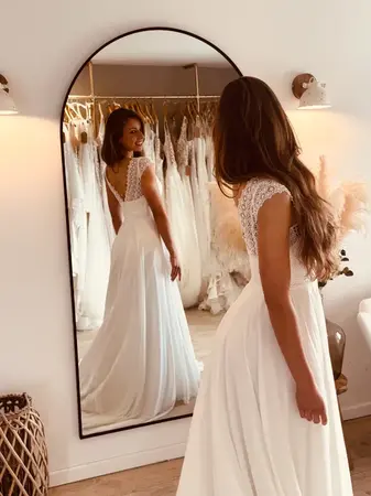 Future mariée essayant une robe de mariée fluide avec dos élégant en dentelle devant miroir à Hazebrouck