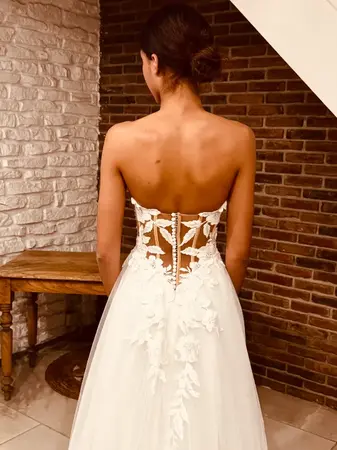 Robe de mariée pas chère en dentelle bohème avec dos lacé et manches transparentes portée en boutique