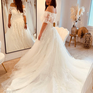 Robe de mariée bohème avec manches en dentelle et jupe légère en tulle portée en boutique près de Béthune