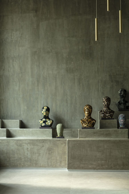 Cement interiors, luxury accessory retail store, clean and minimalist interiors, geometric pedestal display, gold pendant lights, ornamented textured busts