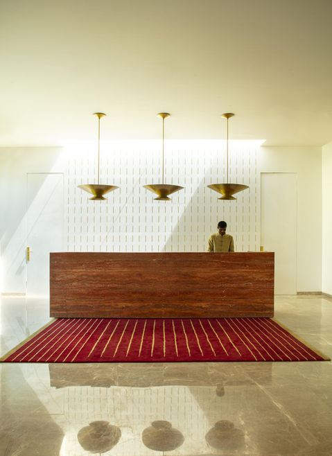 Geometric design for rug, lines in a rug, a reception table in a hotel, suspended ceiling lights in reception area, suspended brass ceiling lights above reception table, suspended traditional Indian ceiling lights, muted design for a reception area in a hotel, marble flooring design in the hotel reception area, hotel reception area minimal backdrop, Buddhism inspired hotel interior design