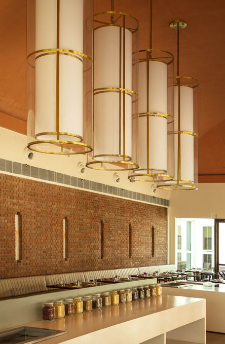 Best all day dining restaurant in India, prayer wheel inspired ceiling lights, vaulted ceiling in a restaurant, double height ceiling restaurants, brick wall cladding, buffet area in a all day dining restaurant, terracotta ceiling, warm restaurant colour palette, cylindrical suspended ceiling lights, white and terracotta mood restaurant interior design, contemporary design for an all day dining restaurant, Buddhism inspired hotel interior design