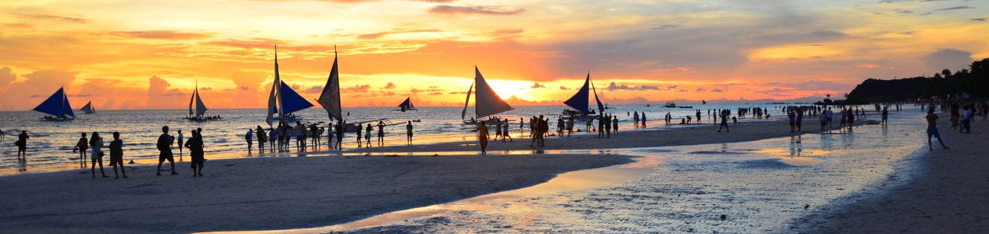 Golden sunset over the beach at Amanpulo resort, Pamalican Island, with silhouettes of guests along the shoreline