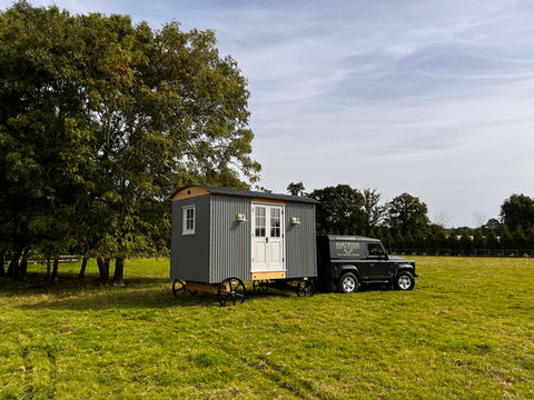 A tiny house on wheels in a field, built by Hartwood Oak in Berkshire, showcasing a cozy and mobile living space.