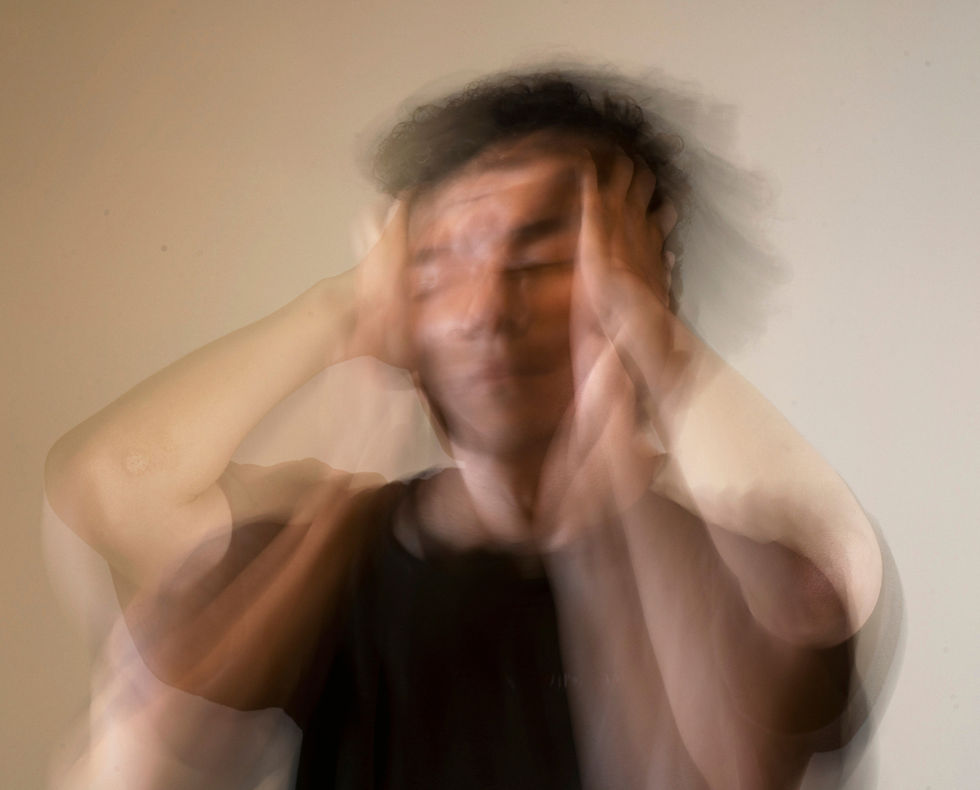 Blurred person holding head in distress, set against a plain background. Motion effect suggests anxiety or confusion.