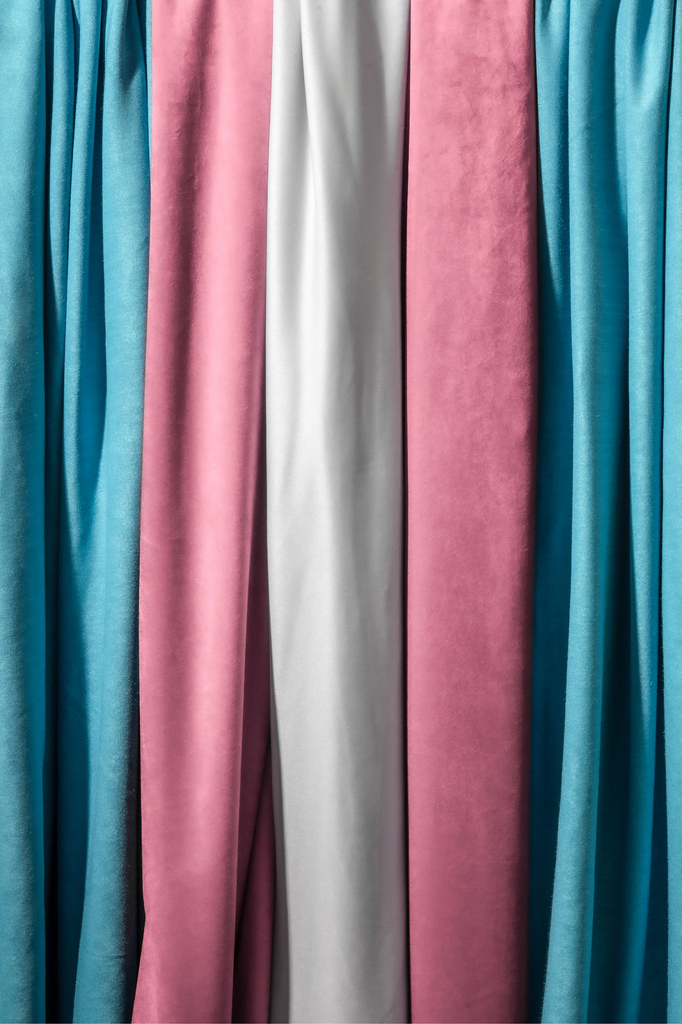 Close-up of vertically hanging fabric in blue, pink, and white stripes. The fabric texture is smooth, creating a calm and soft mood.
