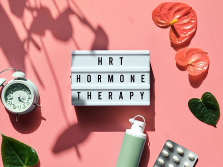 "Lightbox with text 'HRT Hormone Therapy' on pink background. Features an alarm clock, inhaler, pills, and anthurium flowers."