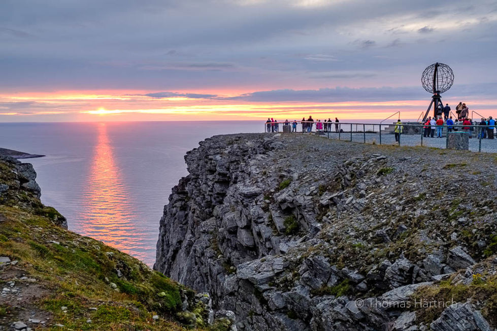 Norwegen, Finnmark. 
Touristen auf dem Felsplateau Nordkap, Insel Magerøya, Plastik der Erdkugel (Globus). Sonnenuntergang über dem Nordmeer.