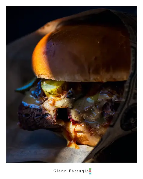 Gourmet burger partially lit in a dark setting showing melted cheese and fillings.