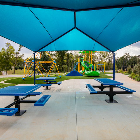 Covered picnic area with blue tables near a colorful playground and green climbing dome.