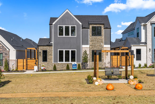Exterior view of a modern two-story home with mixed stone and board-and-batten siding, featuring a wooden pergola swing and fall pumpkins in the front yard.