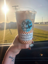 An iced coffee from Coffee Coop with a Bryce Realty Group giveaway label, held up inside a vehicle during sunset as part of LaDonna Jones Bryce's community give-back campaign supporting local businesses.