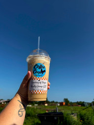 A frozen coffee from Coffee Coop with a Bryce Realty Group giveaway label, held against a bright blue Oklahoma sky during LaDonna Jones Bryce's local business give-back campaign.