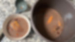 Olla y tazón con caldo de frijoles de color marrón claro, con frijoles cocidos y trozos de plátano visibles, sobre una superficie de cocina. A un lado se observa un cucharón, indicando el proceso de servicio o prueba del caldo.