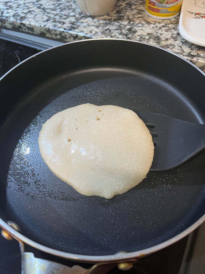 Crepa rústica de avena sin gluten recién vertida en sartén, con la mezcla extendiéndose de forma natural sin formar una lámina muy delgada.