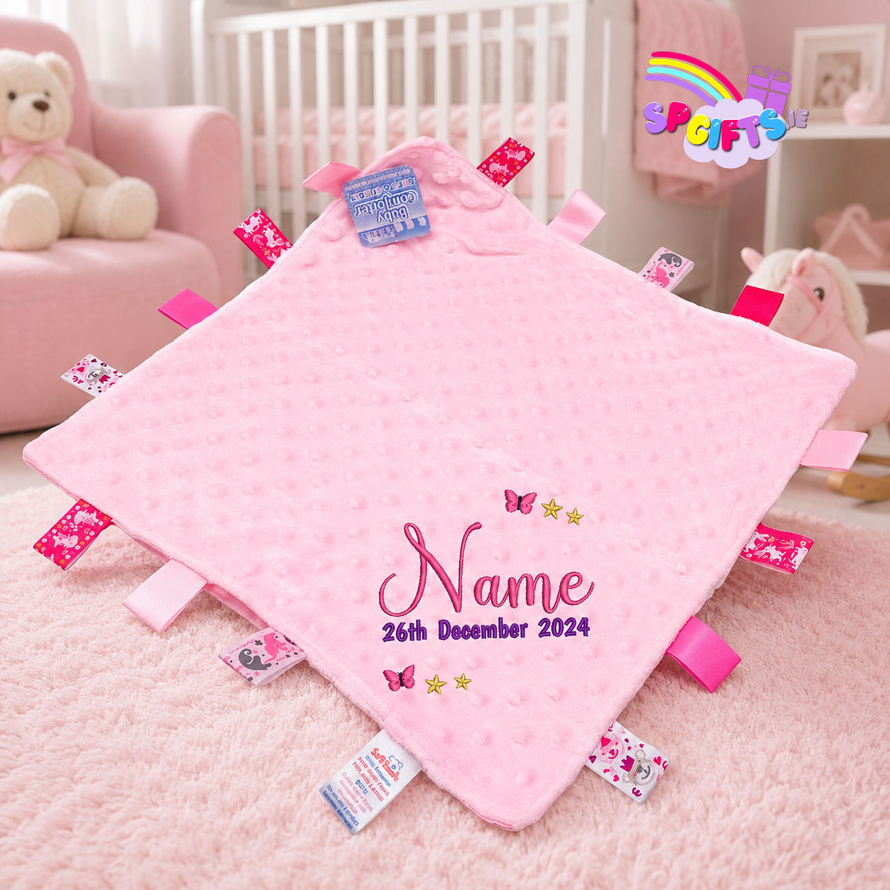 Personalised pink baby taggie blanket with embroidered name and date in a pink nursery setting