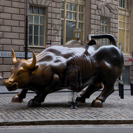 Charging Bull statue on a cobblestone street with buildings in the background.